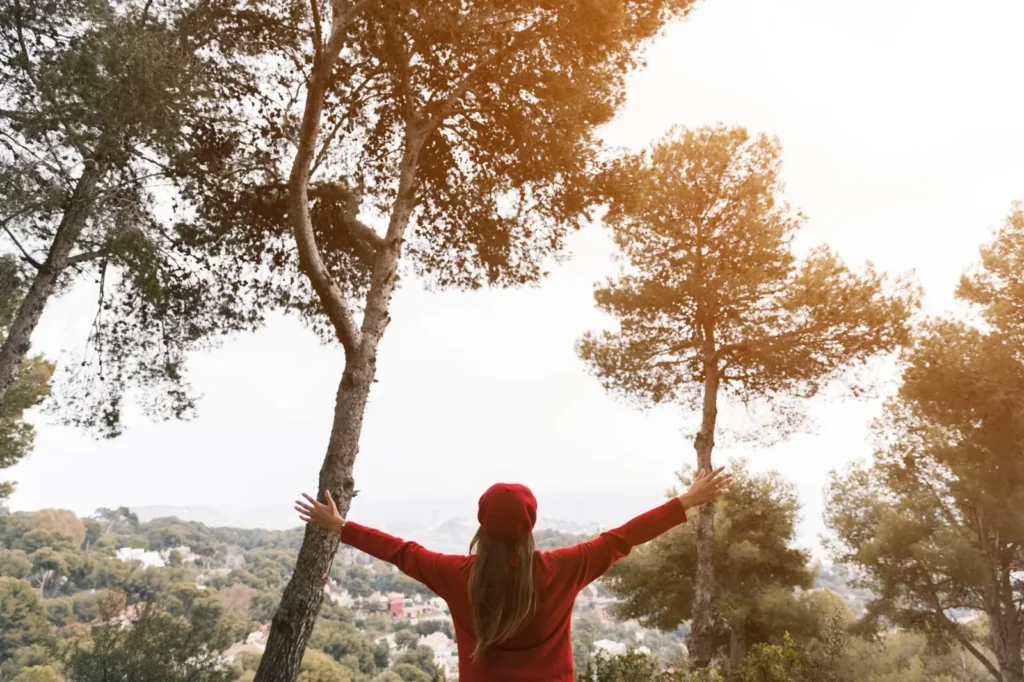 Mulher de braços abertos em meio à natureza, simbolizando o propósito de vida.