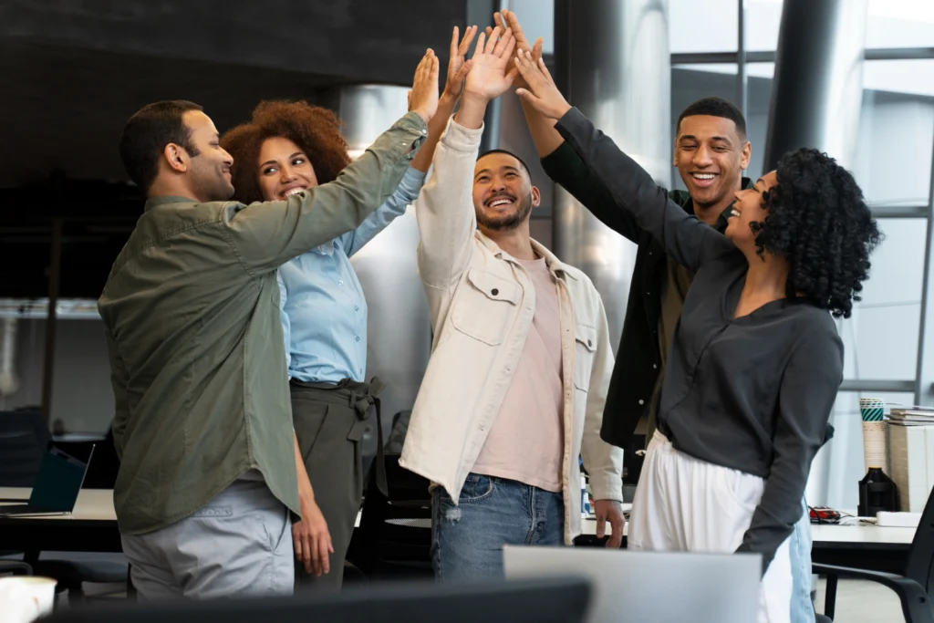 Equipe celebrando resultado no escritório com felicidade no trabalho e engajamento coletivo.
